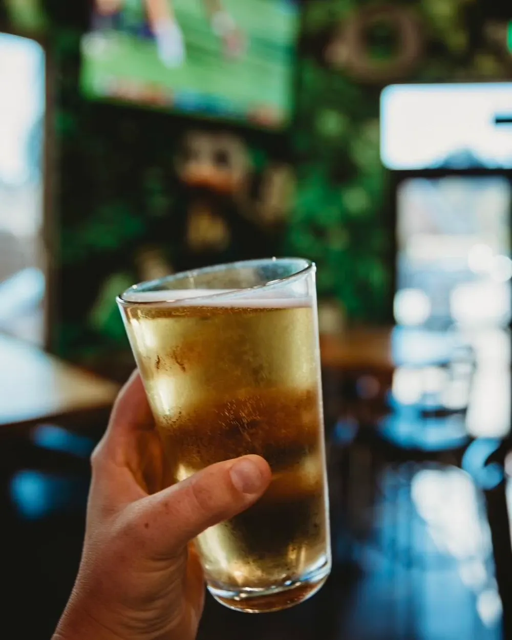 A cold beer raised in the bar, with the game on the TVs behind