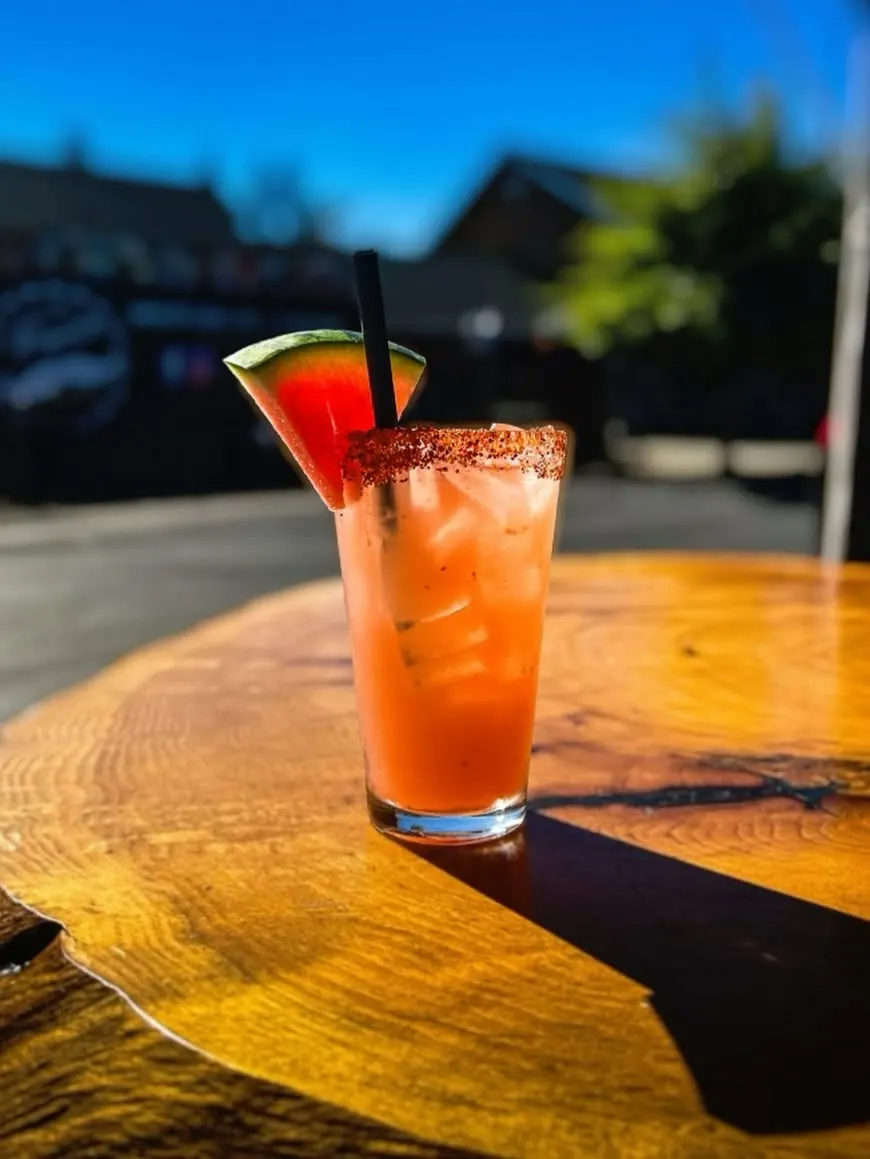 A watermelon cocktail in the sun on a live-edge wood table on the patio